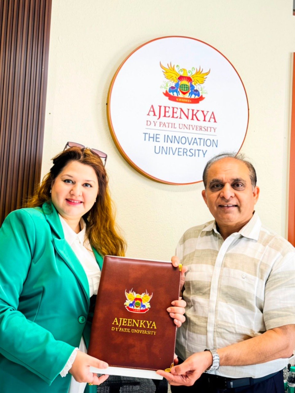 FlyGlam Academy and Ajeenkya DY Patil University representatives holding a university folder